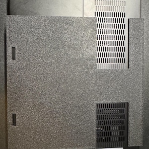 Puede incluir: Base de portátil negra con un panel gris texturizado. El panel tiene dos recortes rectangulares y cubre una sección con ranuras de ventilación. El logotipo de Lenovo es visible en la parte inferior.