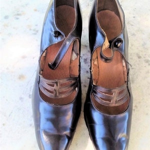 May include: A pair of black leather shoes with a pointed toe and a strap across the instep. The shoes have a decorative cut-out design on the strap.