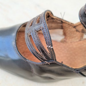May include: Close-up of a black leather shoe with a cut-out design on the strap. The shoe has a pointed toe and a low heel.