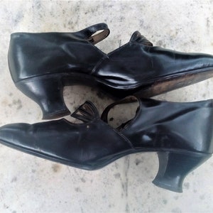 May include: A pair of black leather heeled shoes with a strap and buckle detail. The shoes have a pointed toe and a low heel.