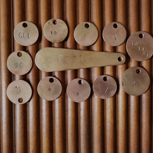 Könnte beinhalten: Eine Sammlung von Messing-Etiketten mit verschiedenen Zahlen und Buchstaben, darunter "CEL", "UC", "10", "7", "9", "11 & 12", "6", "8", "9.", und "FCTB".