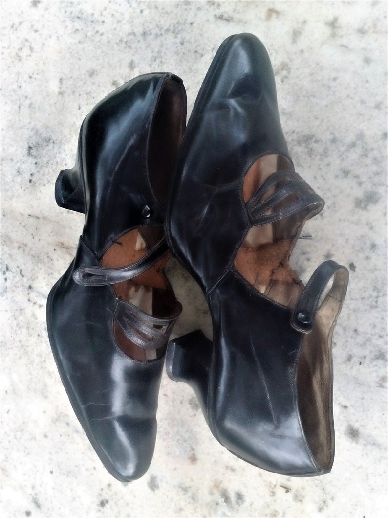 May include: A pair of black leather heeled shoes with a strap detail and a pointed toe.