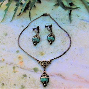 Peut inclure: Ensemble de bijoux vintage comprenant un collier et des boucles d'oreilles assorties. L'ensemble pr&eacute;sente une finition en m&eacute;tal fonc&eacute; avec des d&eacute;tails de filigrane orn&eacute;s. Chaque pi&egrave;ce met en valeur une pierre de couleur turquoise, orn&eacute;e de petites perles blanches et de strass transparents.