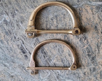 Puede incluir: Dos hebillas de latón antiguas con un diseño sencillo. Las hebillas están hechas de un metal liso y brillante y tienen una forma ligeramente redondeada.