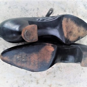 May include: A pair of black leather shoes with worn leather soles. The shoes have a pointed toe and a low heel.