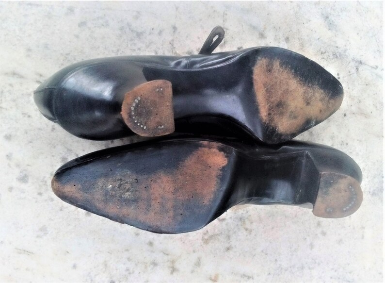 May include: A pair of black leather shoes with worn leather soles. The shoes have a pointed toe and a low heel.