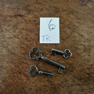 May include: Three antique keys with ornate designs, including a heart-shaped keyhole, on a wooden surface. A white note with the text "16 TK" is in the top right corner of the image.