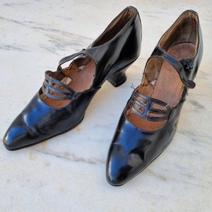 May include: A pair of black leather heeled shoes with a strap across the instep and a decorative cut-out design.