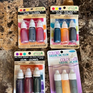 May include: Four blister packs of Life of the Party liquid colorants for bath and body bases. Each pack contains three small plastic squeeze bottles with white caps. The sets include various colors like orange, wine, gold, red, yellow, blue, lilac, peach, seafoam, turquoise, and lime, with volumes of 0.25 fl oz or 0.30 fl oz per bottle.