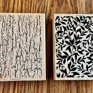 May include: Two wooden stamps. One features a bark texture in black on a light background. The other stamp has a black leaf pattern on a light background. Both stamps are rectangular.