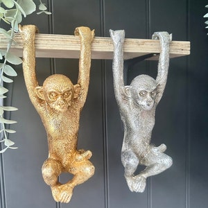 May include: Two monkey figurines hanging from a shelf. One monkey is gold and the other is silver.