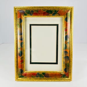 May include: A rectangular picture frame featuring a gold-toned outer border and an inner frame decorated with a colorful pattern of red, orange, green, and blue circular shapes. The frame includes a cream-colored mat and a dark green inner border.