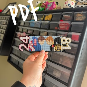 May include: A cross-stitch piece featuring the numbers "24" and "18" in a pixelated design. The "24" is pink and white, the center section is blue and brown, and the "18" is yellow and black. The word "PDF" is written in white.