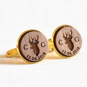May include: A pair of gold cufflinks with a wooden inlay featuring a deer silhouette and the initials "C G" and the date "12.04.2018".