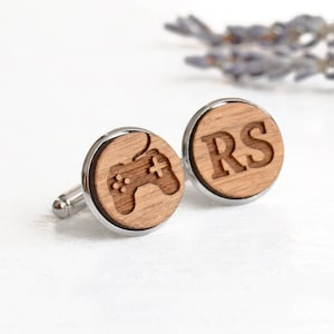 May include: A pair of wooden cufflinks with a silver metal backing. One cufflink features a laser-engraved image of a video game controller. The other cufflink features the initials "RS" engraved in a bold font.