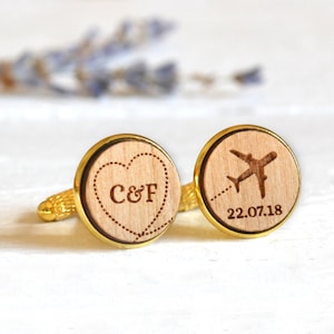 Puede incluir: Un par de gemelos de oro con un corazón de madera grabado con "C&F" y un avión de madera grabado con "22.07.18".