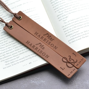 Puede incluir: Dos marcadores de cuero marrón con texto en relieve. Uno dice "Mrs HARRISON", el otro "Mr HARRISON". El segundo marcador tiene las iniciales "L & J" y la fecha "28.08.24". Cada marcador tiene un cordón marrón.