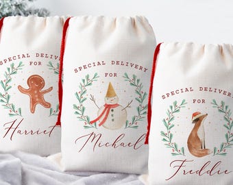May include: Three off-white drawstring gift bags with red cords. Each bag features a watercolor illustration and the words "Special Delivery For" above a name. Designs include a gingerbread man, a snowman, and a fox.
