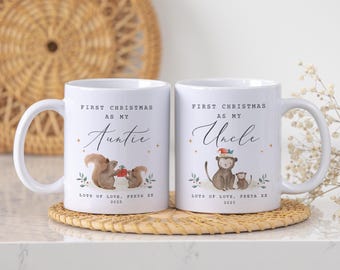 May include: Two white ceramic mugs with curved handles. One mug reads "First Christmas as my Auntie" with a squirrel illustration. The other mug reads "First Christmas as my Uncle" with a monkey illustration. Both mugs have the text "Lots of Love, Freya XX 2025".
