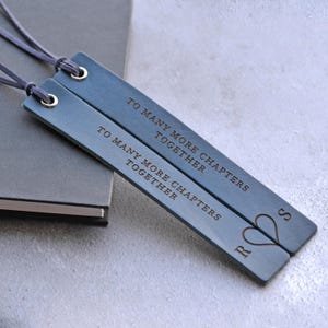 Puede incluir: Dos marcapáginas de cuero azul con el texto grabado "TO MANY MORE CHAPTERS TOGETHER". Cada marcapáginas tiene un ojal dorado y un cordón azul a juego. Un marcapáginas tiene las iniciales "R" y "S" con un símbolo de corazón.