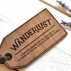 May include: A wooden tag with the word "WANDERLUST" engraved in a decorative font. The tag also includes the text "A strong desire for or impulse to wander or travel and explore the world."