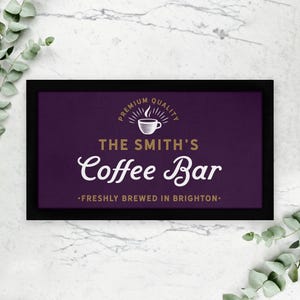 Puede incluir: Un letrero enmarcado en negro con fondo morado y letras doradas. El letrero dice "Premium Quality" con un icono de taza de café, "The Smith's Coffee Bar", y "Freshly brewed in Brighton."
