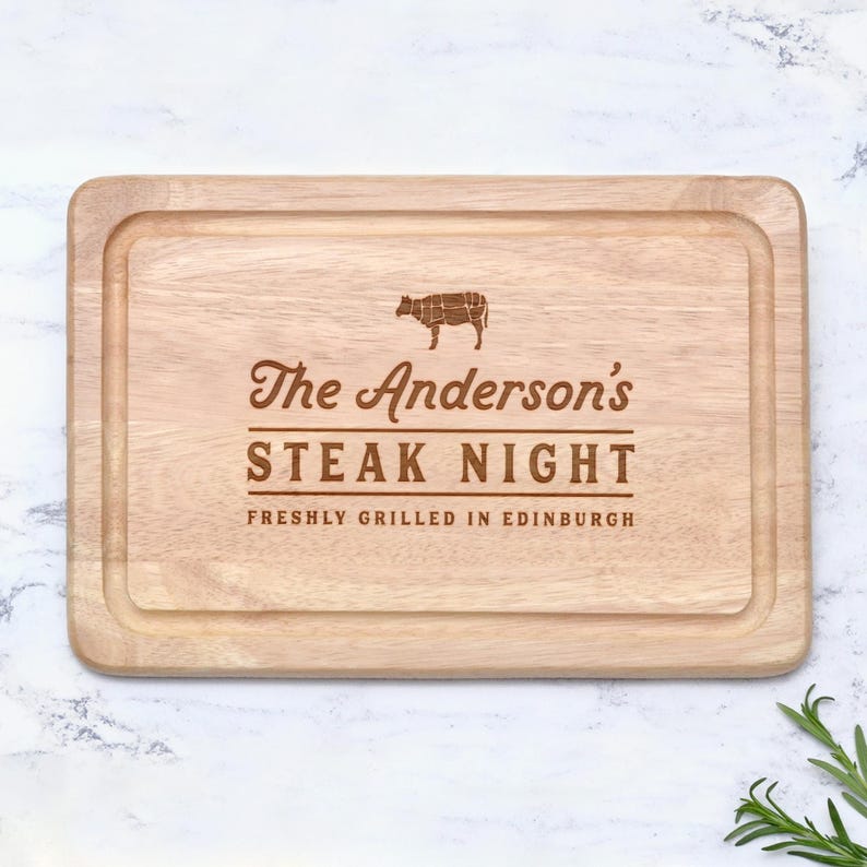 K&ouml;nnte beinhalten: Rechteckiges Holzschneidebrett mit geschnitztem Rand. Der Text "The Anderson's STEAK NIGHT" ist in einer dekorativen Schriftart eingraviert, zusammen mit einem Diagramm einer Kuh und dem Satz "FRESHLY GRILLED IN EDINBURGH".