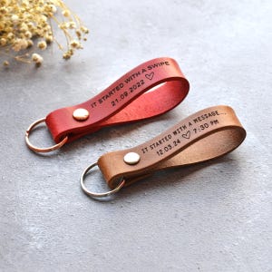 May include: Two leather keyrings, one red and one brown, with metal rings. The red keyring reads "IT STARTED WITH A SWIPE 21.09.2022". The brown keyring reads "IT STARTED WITH A MESSAGE... 12.03.24 7:30 PM".