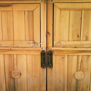 May include: Two wooden doors with black metal handles and a silver latch. The doors are made of horizontal planks and have a light brown color.