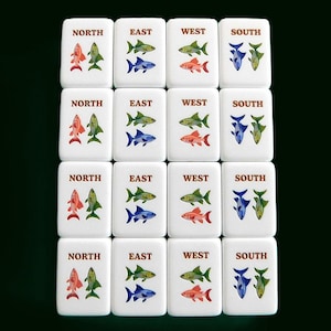 Peut inclure: Ensemble de tuiles de Mahjong blanches, chacune portant une direction cardinale : Nord, Est, Ouest et Sud. Chaque tuile pr&eacute;sente un motif de poissons color&eacute;s en rouge, vert, bleu et jaune.