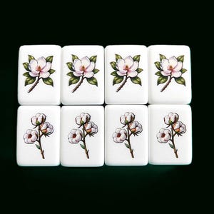 Peut inclure: Huit carreaux blancs avec des motifs floraux. La rang&eacute;e sup&eacute;rieure pr&eacute;sente des fleurs de magnolia avec des feuilles vertes, tandis que la rang&eacute;e inf&eacute;rieure affiche des brins de coton avec des boules blanches duveteuses. Les carreaux sont dispos&eacute;s sur un fond vert fonc&eacute;.