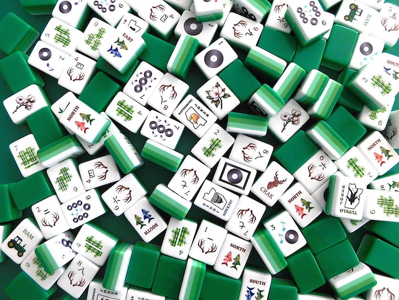 Peut inclure: Vue a&eacute;rienne d'une collection de tuiles de Mahjong blanches et vertes. Les tuiles pr&eacute;sentent divers symboles, chiffres et caract&egrave;res, notamment du bambou, des fleurs et des cerfs. Les tuiles vertes sont rectangulaires et entourent les tuiles blanches.