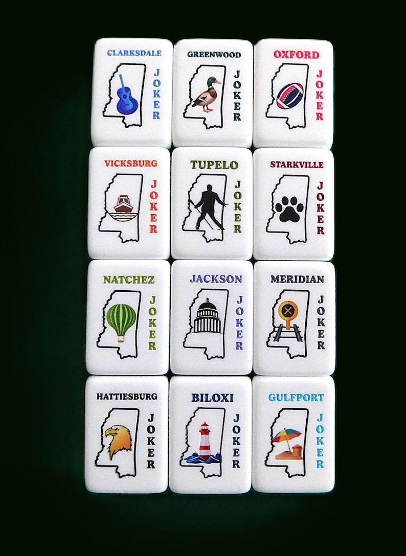 Peut inclure: Ensemble de tuiles blanches avec des illustrations et des noms de villes du Mississippi, dont Clarksdale, Greenwood, Oxford, Vicksburg, Tupelo, Starkville, Natchez, Jackson, Meridian, Hattiesburg, Biloxi et Gulfport. Chaque tuile porte le mot "JOKER" en rouge.