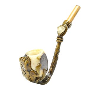 May include: A hand-carved wooden pipe with a frog design. The pipe is made of light brown wood and has a white bowl. The stem is made of bamboo and has a clear crystal at the end.