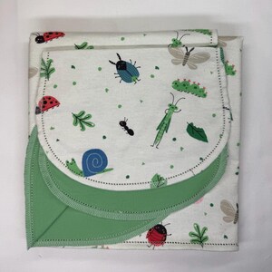 May include: A folded fabric item featuring an off-white background with a repeating pattern of colorful insects including ladybugs, a blue snail, a green grasshopper, and moths, finished with a solid sage green border and stitched edges.