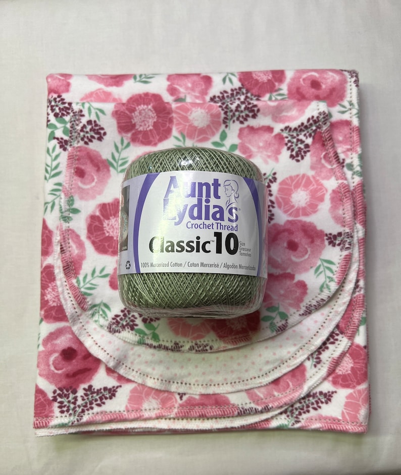 Puede incluir: Una bola de hilo de crochet Aunt Lydia's Classic 10 de color verde con texto blanco sobre un fondo de tela floral rosa y blanco.