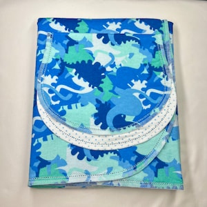 May include: A blue and green patterned baby blanket with a white trim and a scalloped edge. The blanket is folded in thirds and has a white polka dot pattern on the inside.