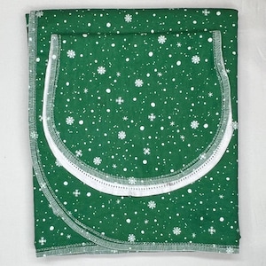 May include: A green fabric Christmas tree skirt with a white snowflake and dot pattern. The skirt has a white trim around the edge.
