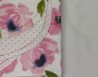 May include: A white fabric featuring a pink floral pattern with dark centers and green leaves. The fabric has a scalloped edge with a pink polka dot border and a delicate stitched hem detail, showcasing a layered textile design with soft textures.