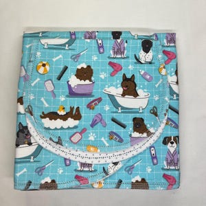 May include: A blue fabric wrap with a white border and a repeating pattern of dogs in a bathtub, dog grooming tools, and bones. The fabric is folded in half and the pattern is visible on both sides.