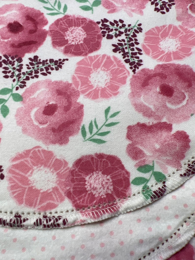 Puede incluir: Una tela blanca con un patr&oacute;n floral rosa. La tela tiene un borde festoneado y est&aacute; doblada sobre s&iacute; misma.