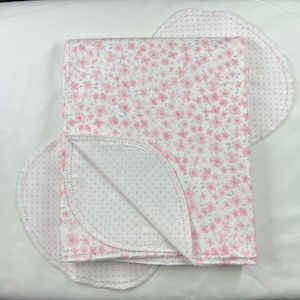May include: A white baby blanket with a pink floral print on one side and a white background with pink polka dots on the other side.