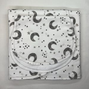 May include: White baby blanket with a gray crescent moon and star pattern. The blanket has a matching bib attached. The blanket is folded and ready for use.