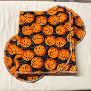 May include: A black and orange fabric with a basketball pattern. The fabric has the words "SLAM", "DUNK", and "HOOP" printed on it.