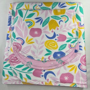 May include: A white fabric with a pink, yellow, blue, and green floral pattern. The fabric is folded in layers and has a scalloped edge.