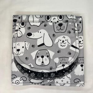 May include: A folded gray baby blanket with a repeating pattern of cartoon dog faces in white and gray. The blanket has a black and white paw print border and a stitched edge.