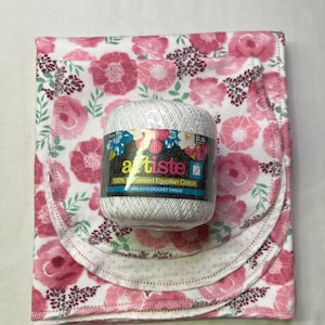 Puede incluir: Una madeja de hilo blanco con un patr&oacute;n floral rosa en la etiqueta. La etiqueta dice "artiste 100% algod&oacute;n egipcio mercerizado 110 yardas #10 Hilo de crochet". La madeja de hilo est&aacute; sobre tres cuadrados de tela floral rosa.