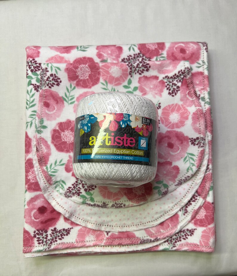 Puede incluir: Una madeja de hilo blanco con un patr&oacute;n floral rosa en la etiqueta. La etiqueta dice "artiste 100% algod&oacute;n egipcio mercerizado 110 yardas #10 Hilo de crochet". La madeja de hilo est&aacute; sobre tres cuadrados de tela floral rosa.