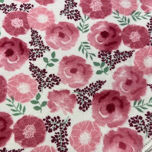 Puede incluir: Una tela blanca con un estampado floral rosa. Las flores son grandes y tienen un efecto acuarela. El fondo es de color crema claro.
