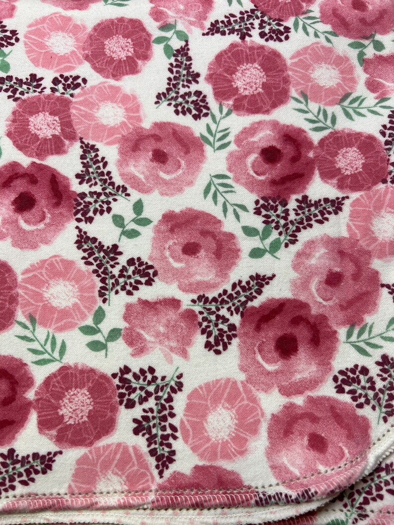 Puede incluir: Una tela blanca con un estampado floral rosa. Las flores son grandes y tienen un efecto acuarela. El fondo es de color crema claro.